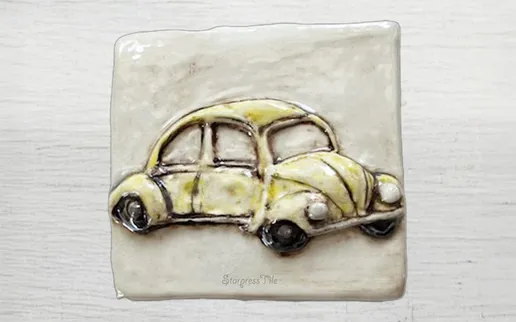 A ceramic tile featuring a yellow vintage car sculpture, highlighting its playful design and textured details. Perfect for decorative use.