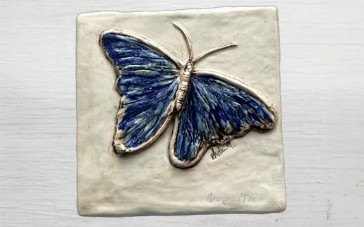 Ceramic tile featuring a detailed relief of a blue butterfly, showcasing vibrant colors and intricate textures, ideal for artistic decor.