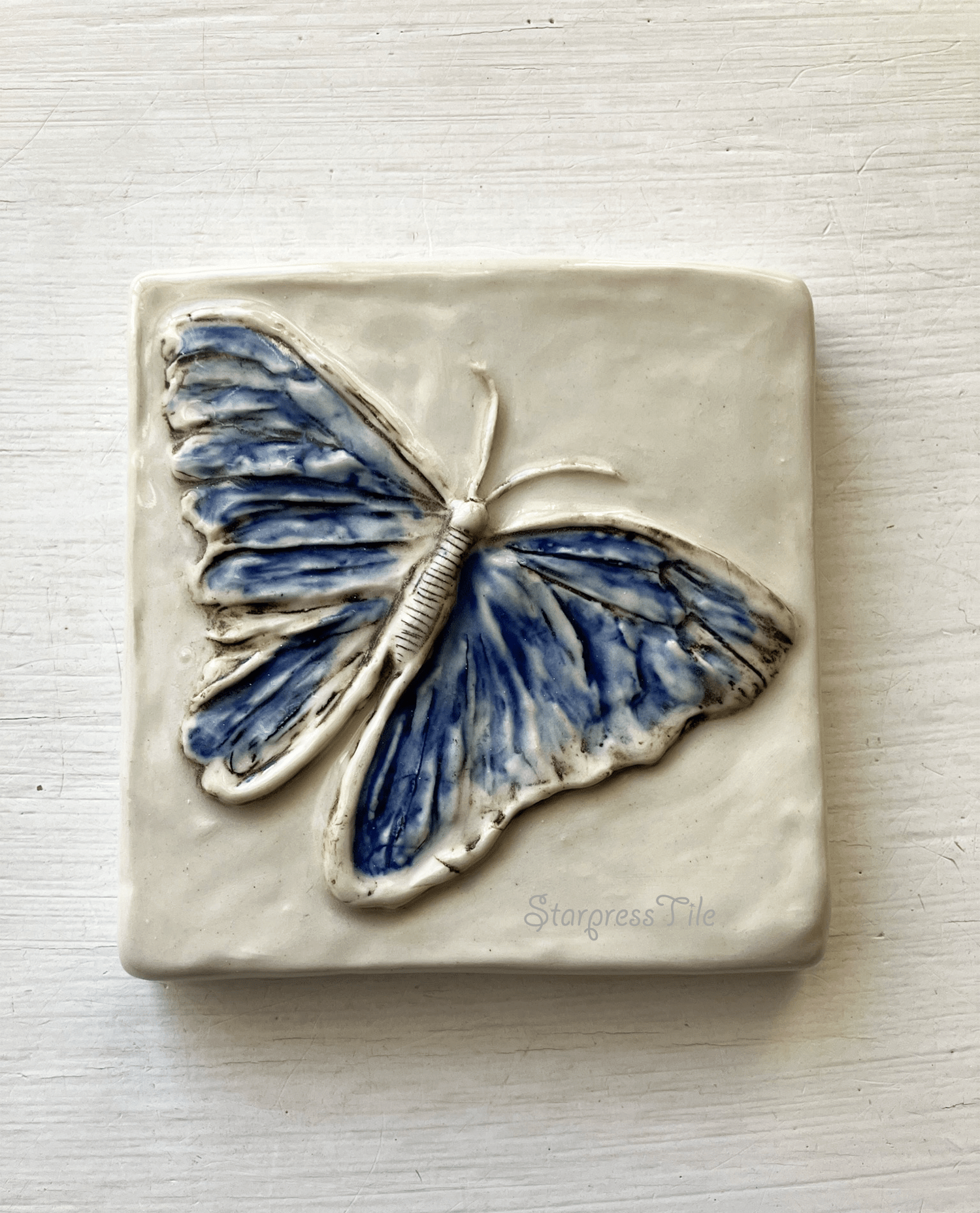 Blue butterfly relief ceramic tile with intricate detailing, featuring a textured white background. Perfect for decor or artistic display.
