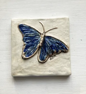 Ceramic tile featuring a detailed blue butterfly design, emphasizing intricate textures and vibrant color, suitable for decorative purposes.