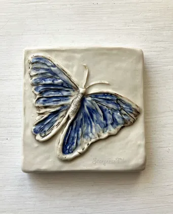 Ceramic tile featuring a blue butterfly relief design. The intricate texture and colors highlight the art's delicate craftsmanship.