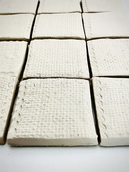 Textured, white clay tiles arranged in a grid pattern, showcasing their detailed surfaces for crafting or artistic projects.
