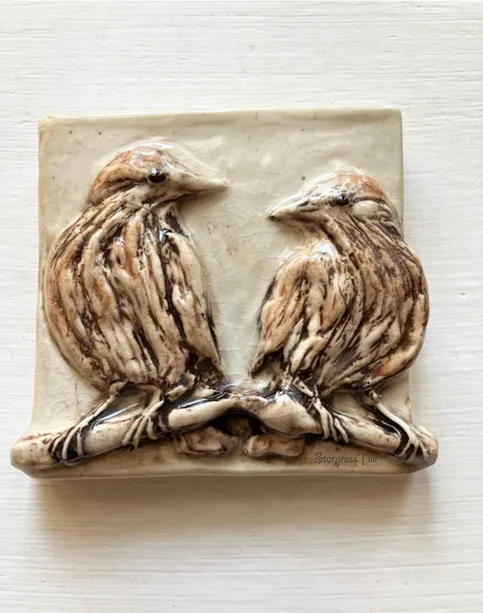 Ceramic relief depicting two birds perched closely on a branch, showcasing detailed textures and earthy tones, ideal for nature-themed decor.