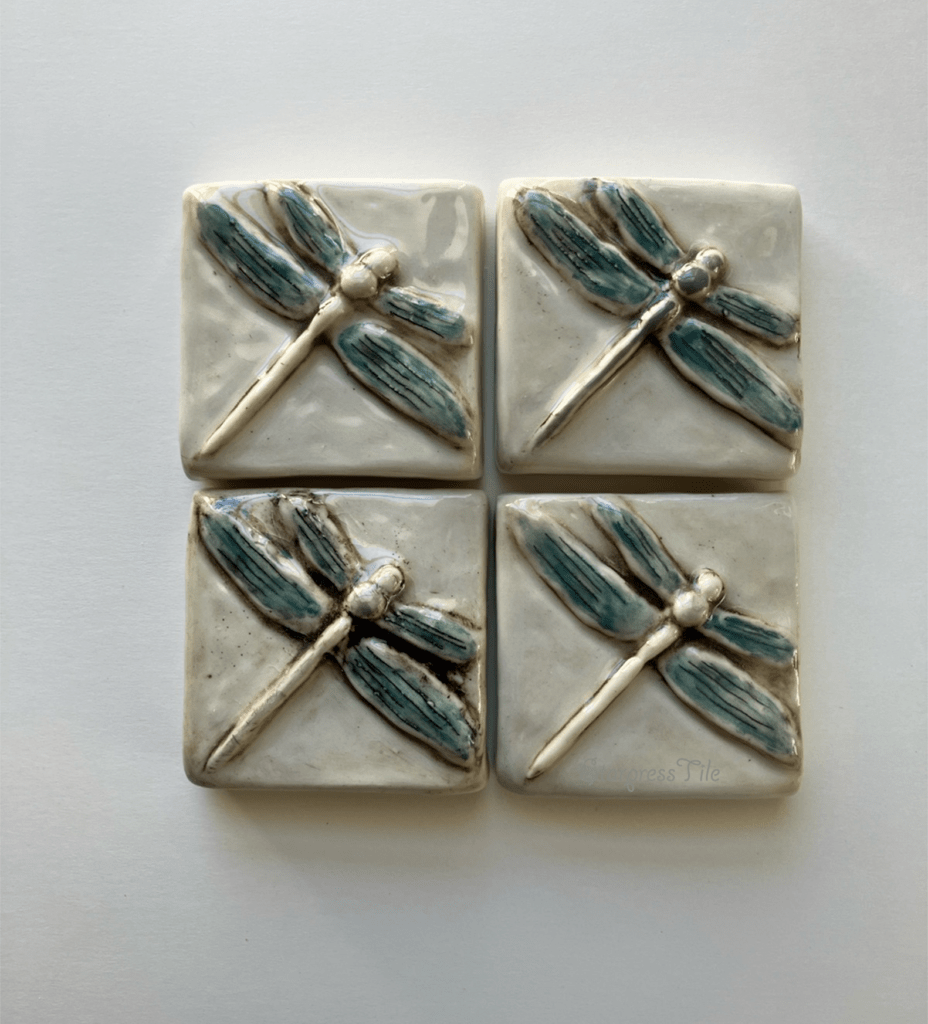 Four ceramic tiles featuring embossed dragonfly designs in a watercolor hand painted teal and brown highlight. The artwork adds a natural element to home decor.